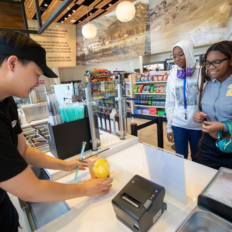 Two students receive their boba drinks from a Lollicup worker.
