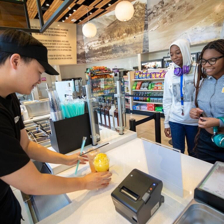 Two students receive their boba drinks from a Lollicup worker.