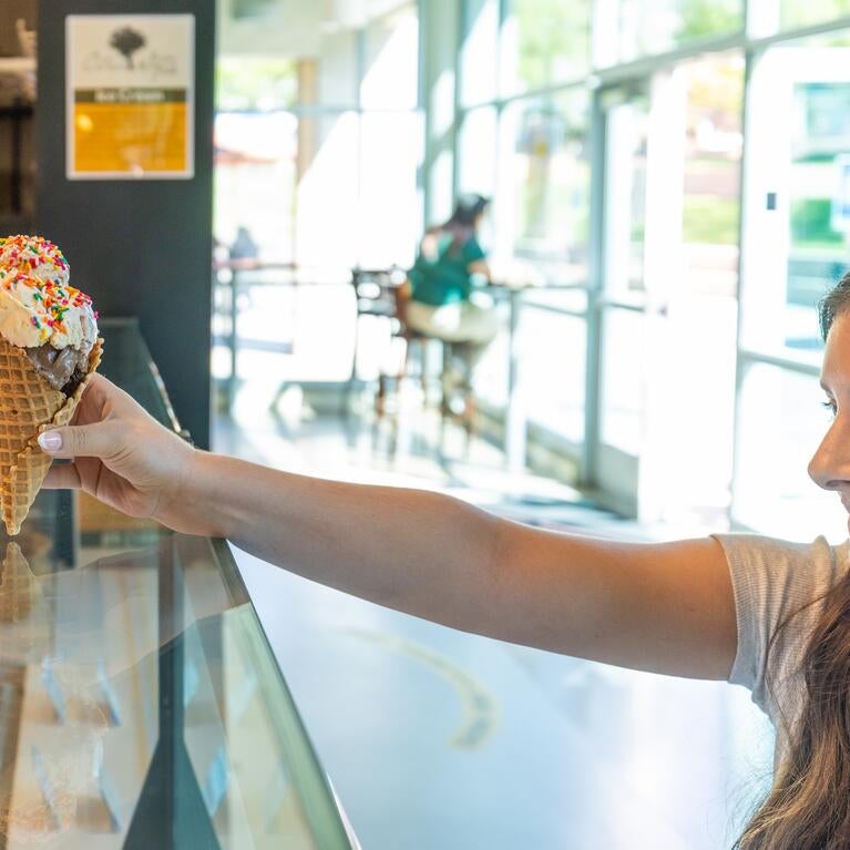 A worker hands a student an ice cream cone from Scoops at the HUB.
