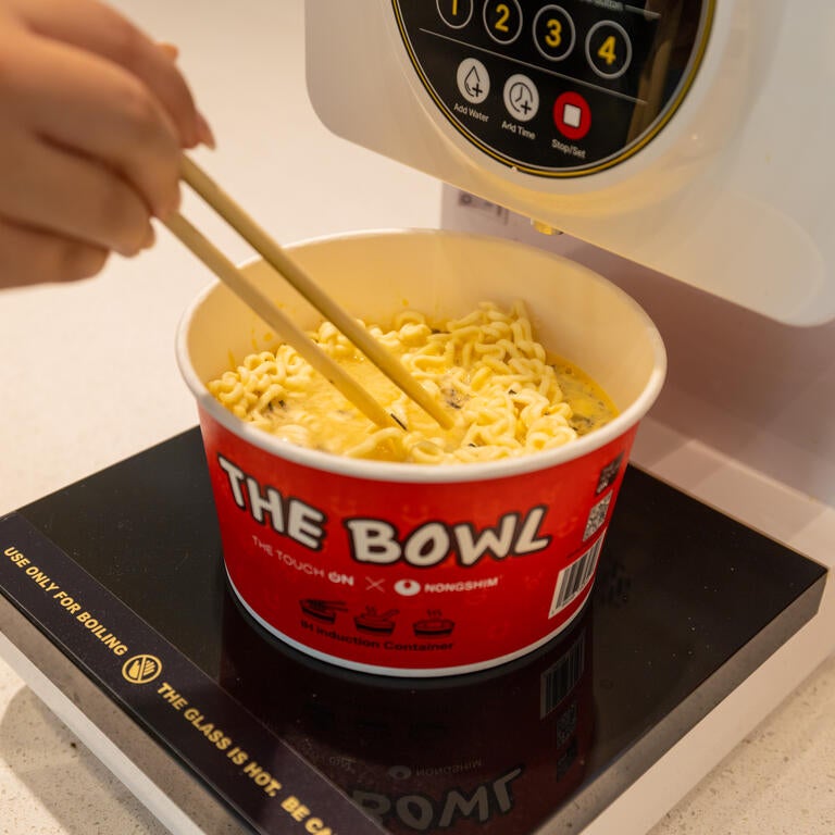 A person uses chopsticks to stir a bowl of ramen as it heats up.