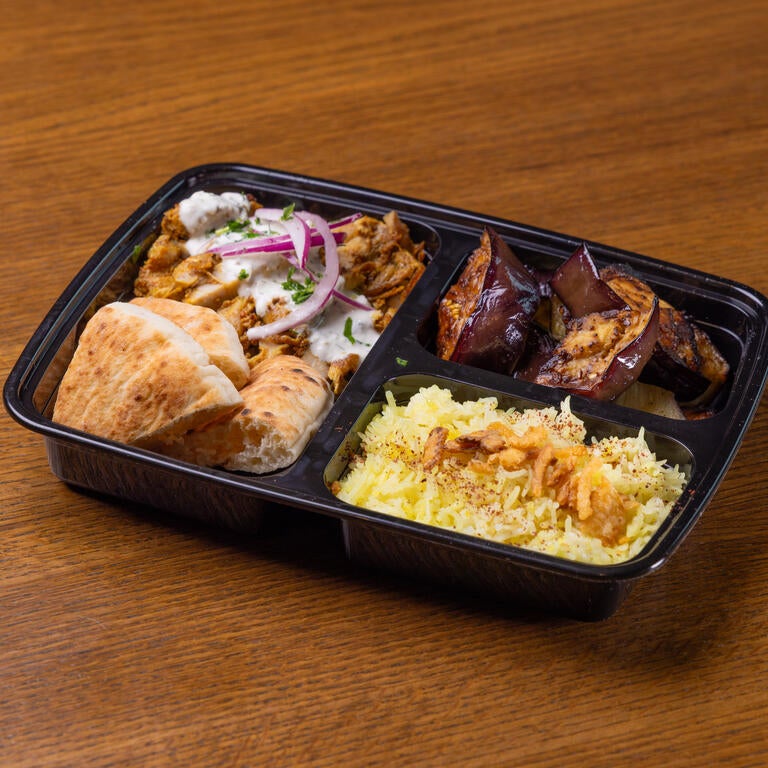 A black to-go box with chicken shawarma and tzatziki sauce, pita wedges, roasted eggplant and saffron basmati rice.