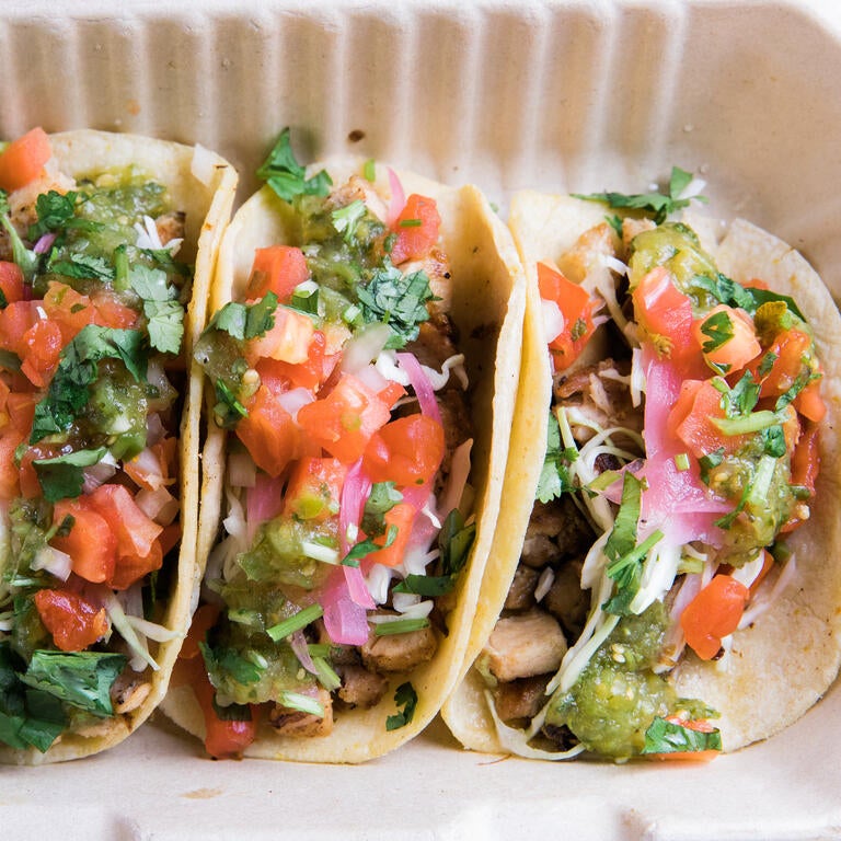 Three steak and chicken street tacos in a disposable container with lime wedges.