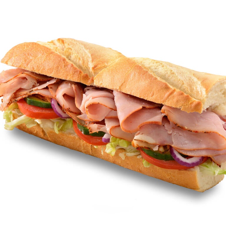 Sub sandwich with ham, tomatoes, cucumbers, lettuce, and onions on white bread.