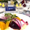 A colorful roasted beetroot salad, featuring dark red and yellow beetroot chunks, garnished with thinly sliced radishes, fresh microgreens and a bright citrus vinaigrette dressing on a white plate.