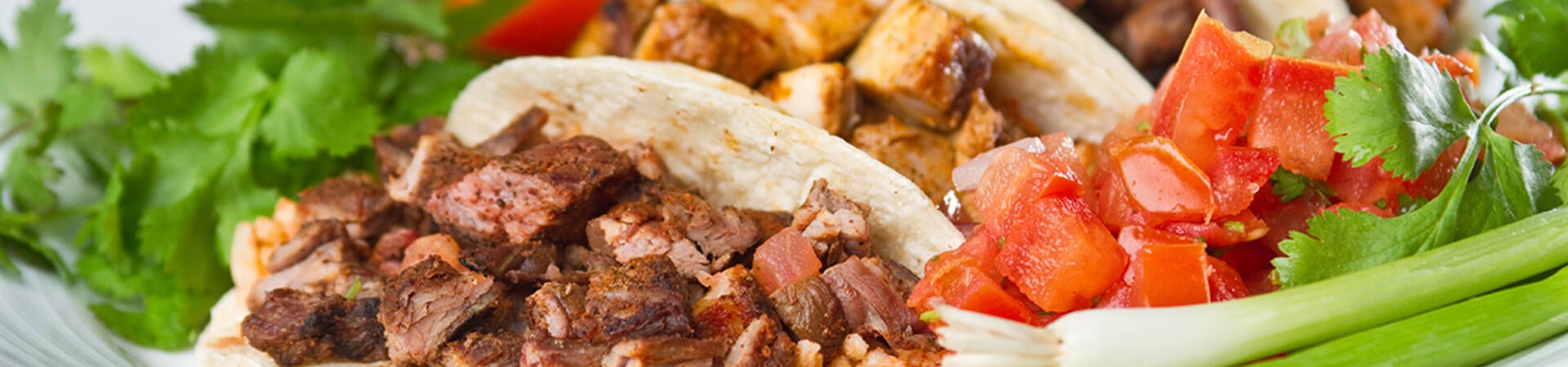 A selection of street tacos with carne asada and pollo meat options, garnished with fresh lettuce and tomatoes.