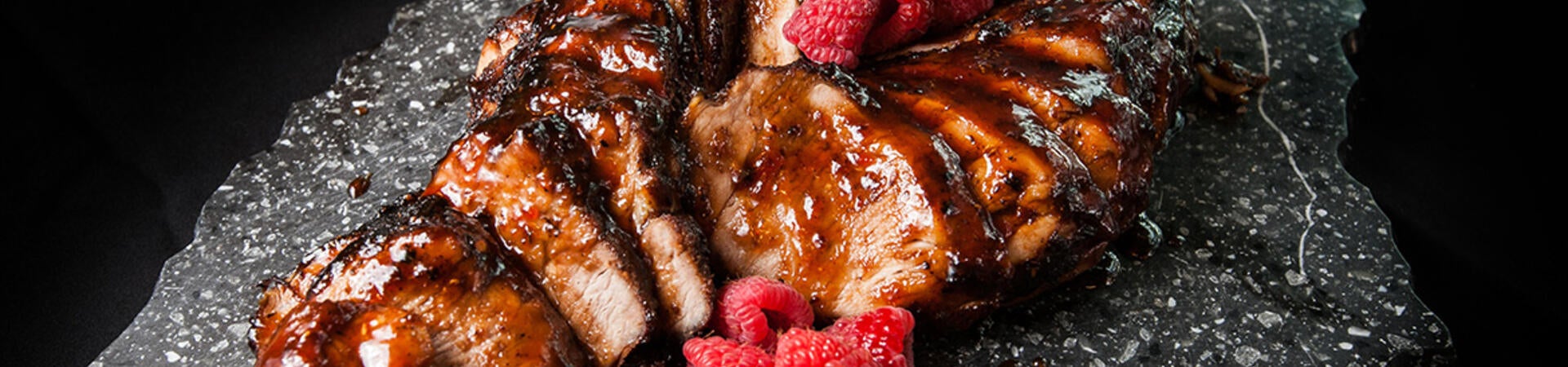 Pork tenderloin served with a dark, savory glaze and fresh raspberries.